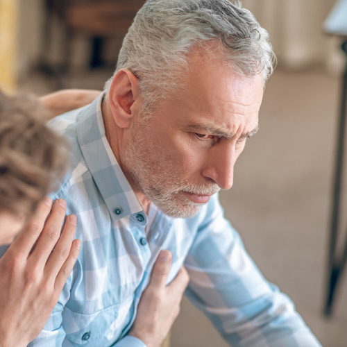Dark-haired male doctor looking after an upset serious gray-headed man suffering from a chest pain