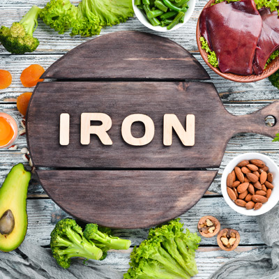 Food containing natural iron. Fe: Liver, avocado, broccoli, spinach, parsley, beans, nuts, on a white wooden background. Top view.