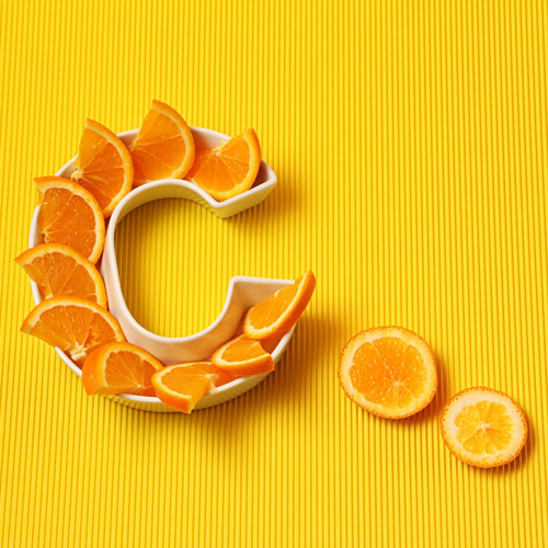 Vitamin C in food concept. Plate in shape of letter C with orange slices on bright yellow background. Ascorbic acid is important for immune system function.